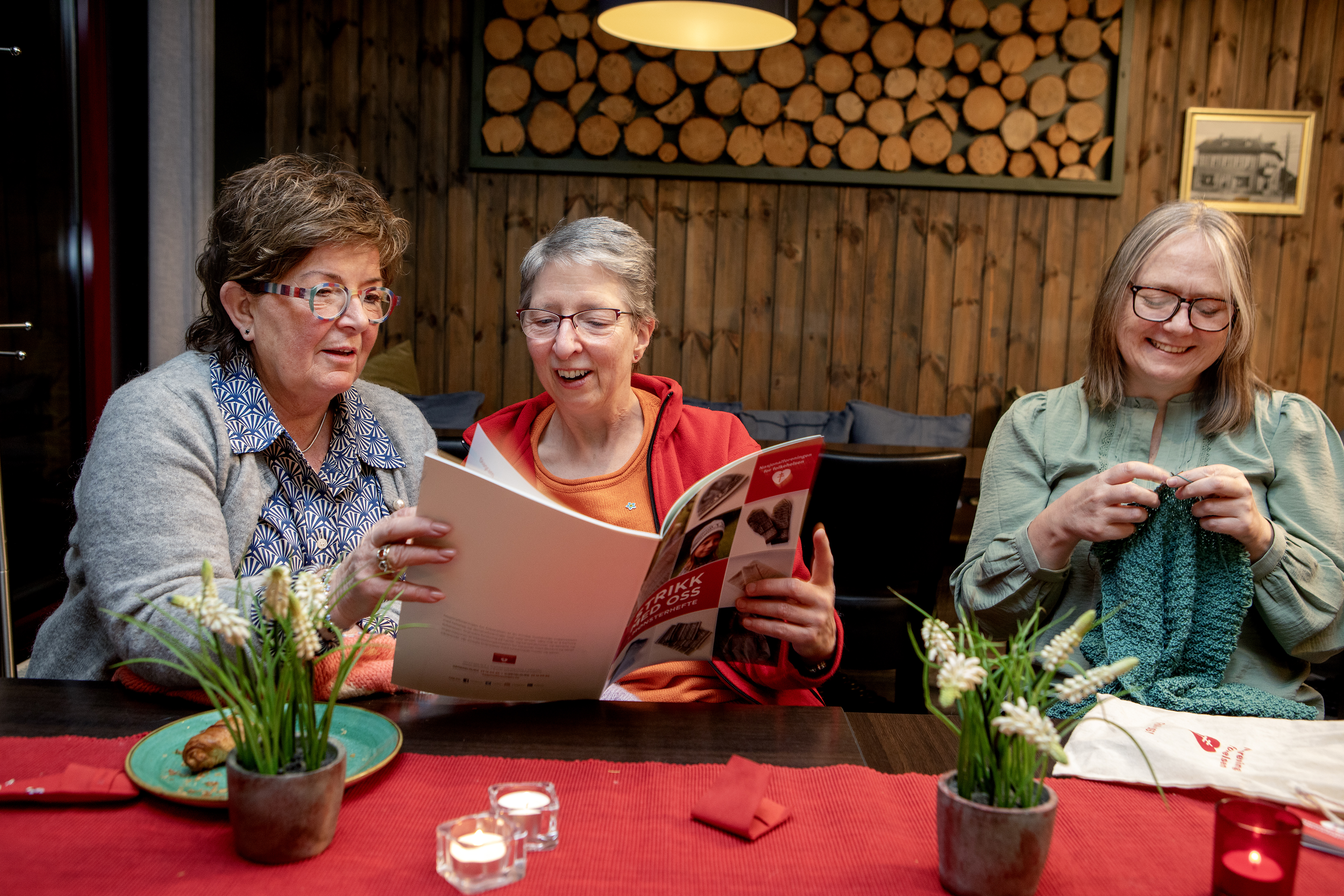 Tre smilende damer som strikker og ser på strikkeoppskrift. 